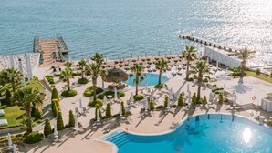 Een zwembad van een resort met uitzicht op zee, omringd door ligbedden en palmbomen.