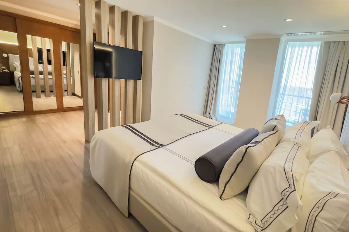 Habitación de hotel con una cama grande, un televisor de pantalla plana en la pared y vistas a la ciudad a través de amplios ventanales.