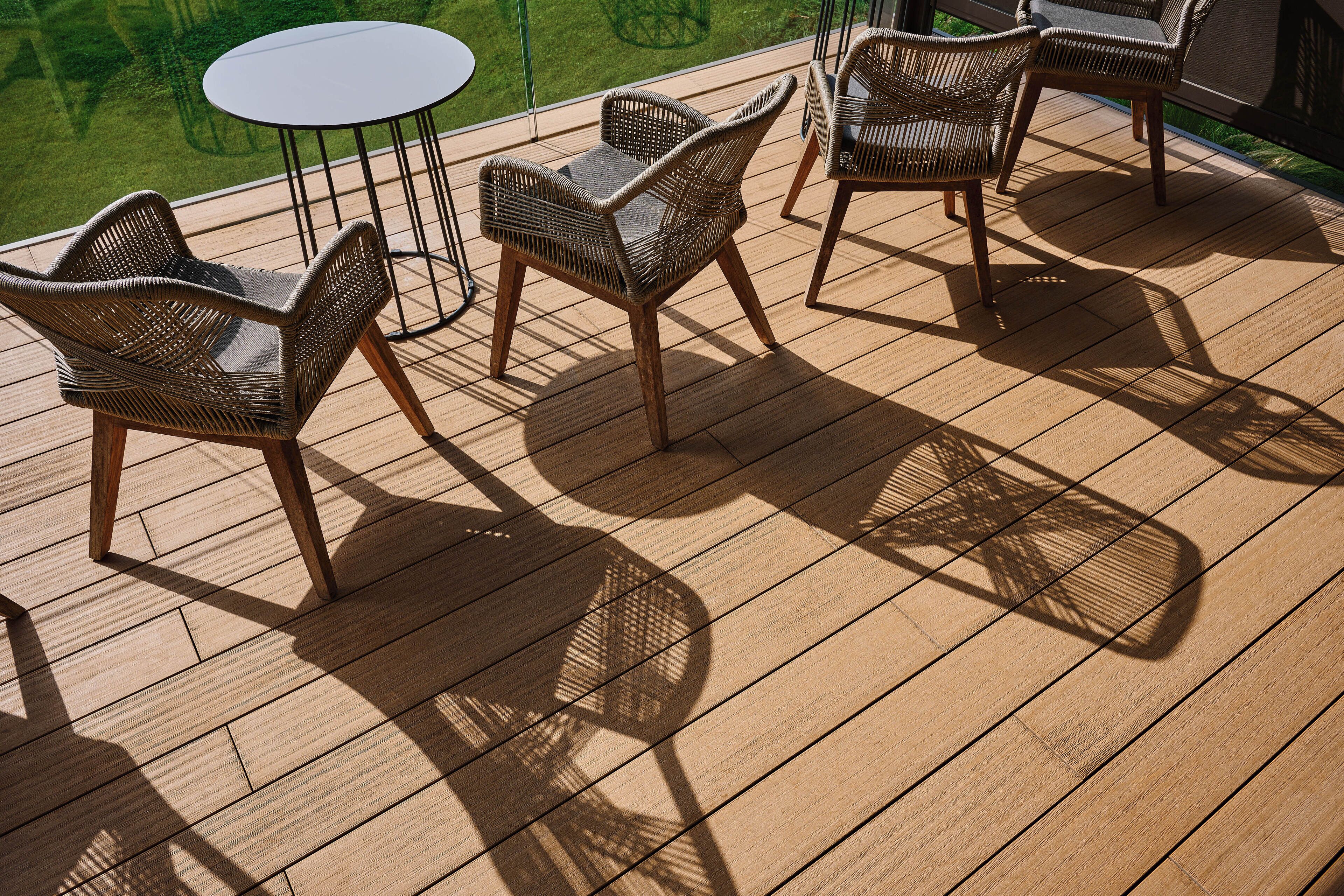 Una terraza de madera con mobiliario de mimbre y una mesa redonda.