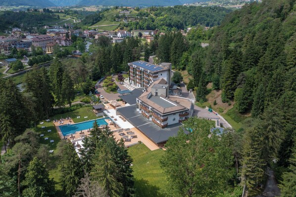 Vista aérea de un hotel con piscina, rodeado de exuberante vegetación y montañas.