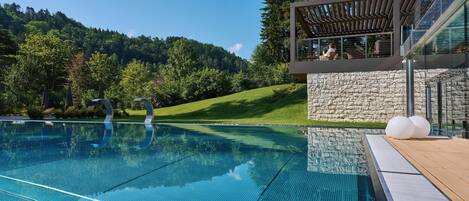 A swimming pool with clear blue water, a stone wall, and a wooden deck.