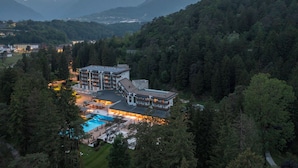 A large resort with multiple buildings, a swimming pool, and surrounded by dense forest and mountains. - Grand Hotel Terme di Comano (Stenico)