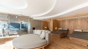 A modern hotel lobby with a large round seating area, wooden panel walls, and a glass entrance leading to a pool area. - Grand Hotel Terme di Comano (Stenico)