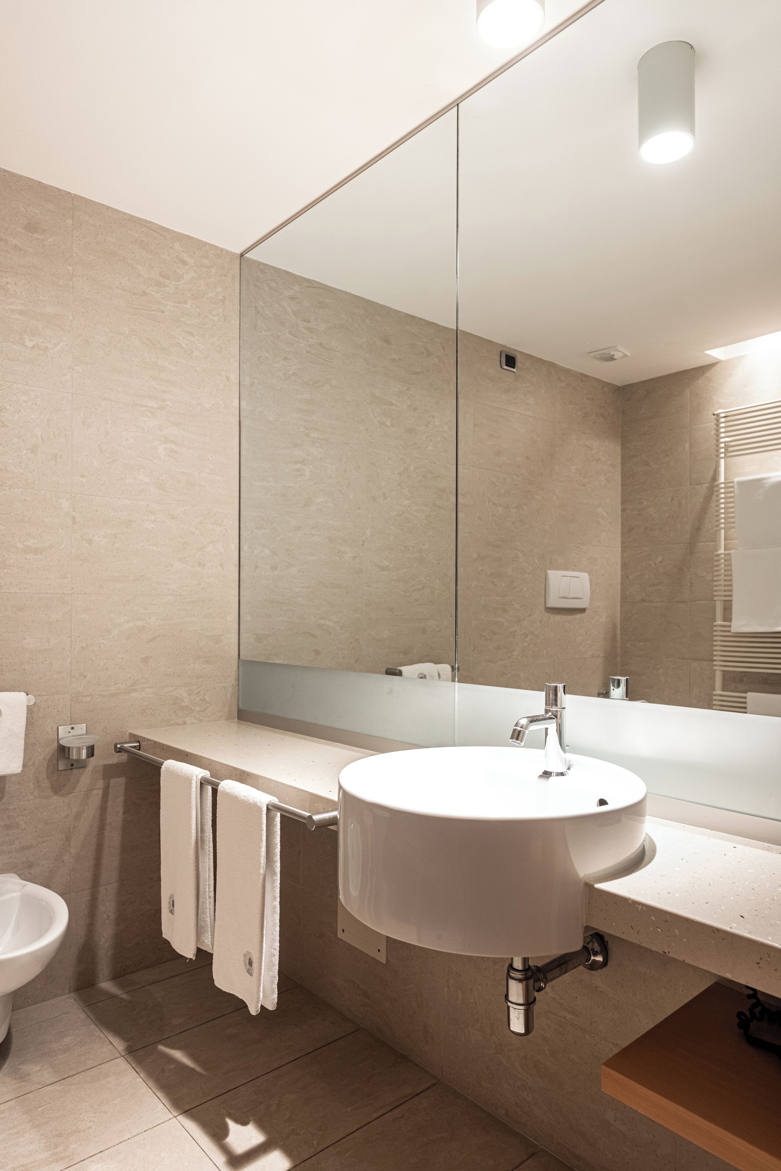 Un baño moderno con un espejo grande, un lavamanos y un inodoro.