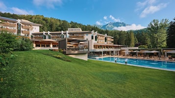 A modern hotel with a pool, outdoor seating, and mountain views.