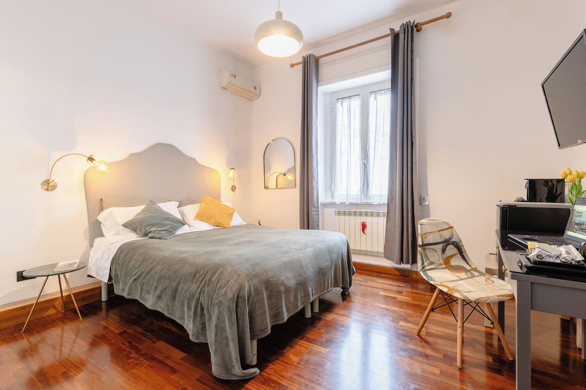 Ein ordentlich eingerichtetes Schlafzimmer mit Bett, Nachttisch, Lampe und Schreibtisch mit Stuhl.