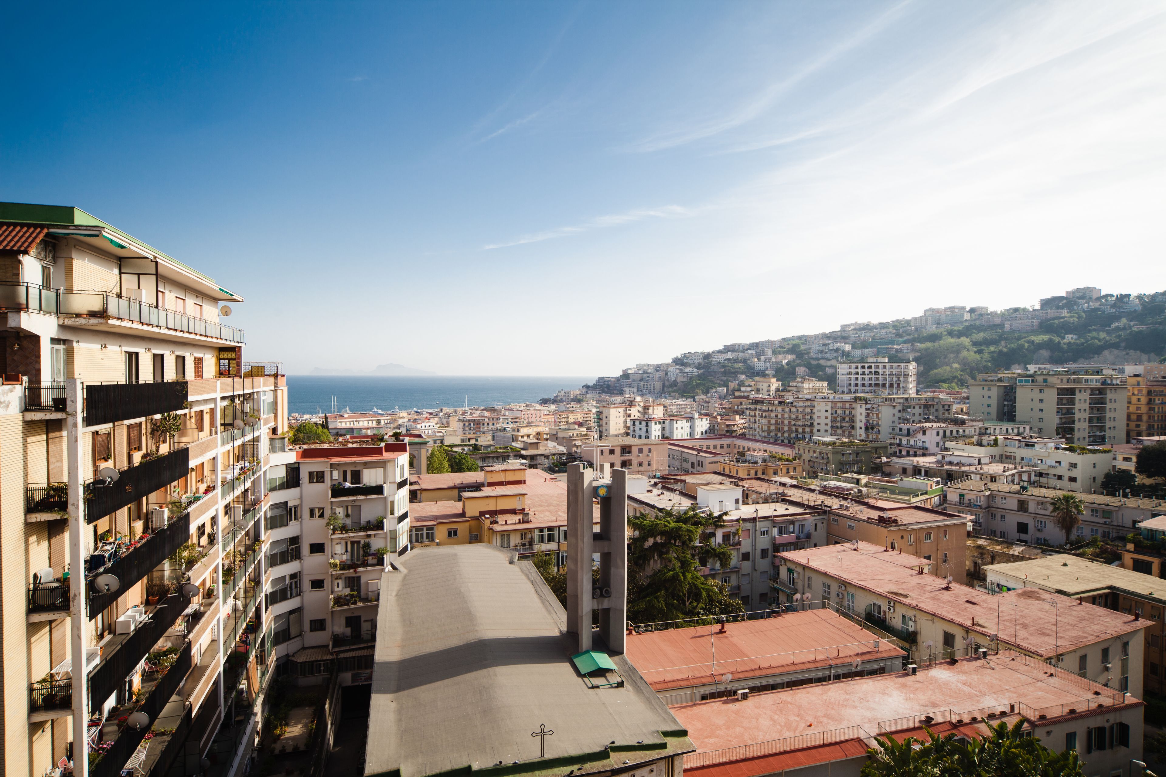 A high-rise building with multiple balconies, a rooftop terrace, and a view of the cityscape and sea.