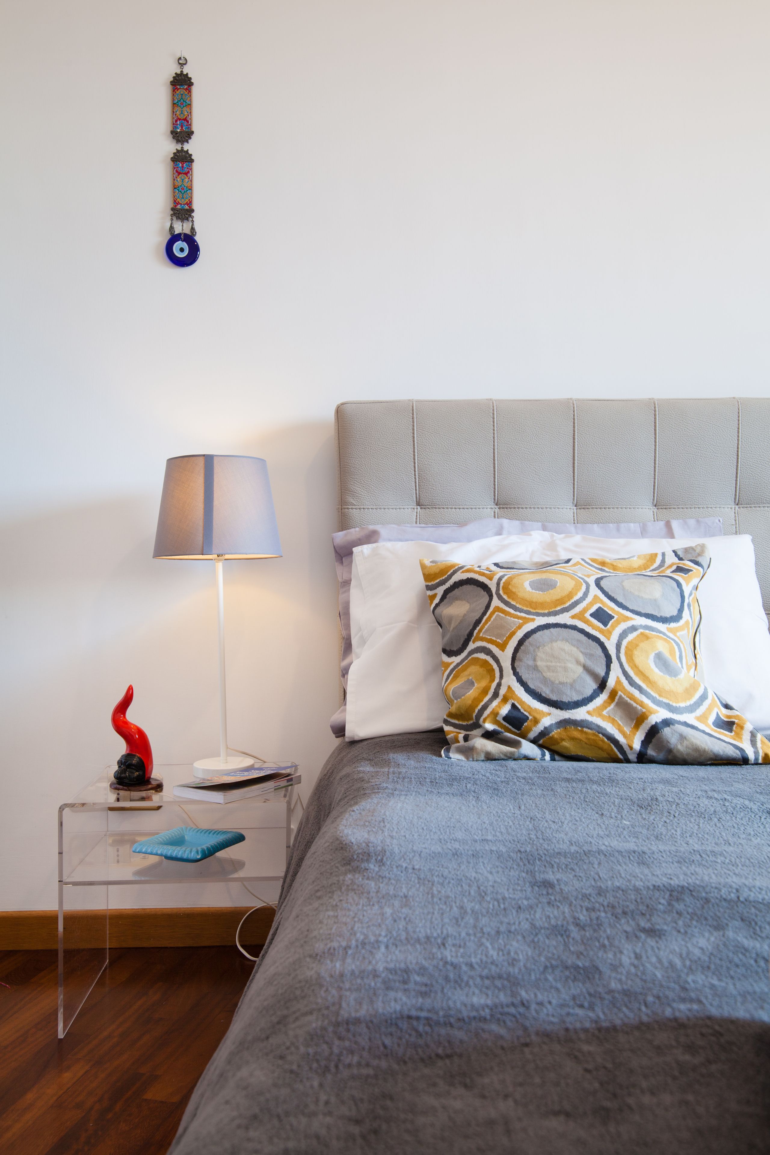 Une chambre à coucher bien rangée, avec un lit, une table de chevet dotée d’une lampe et un objet décoratif accroché au mur.