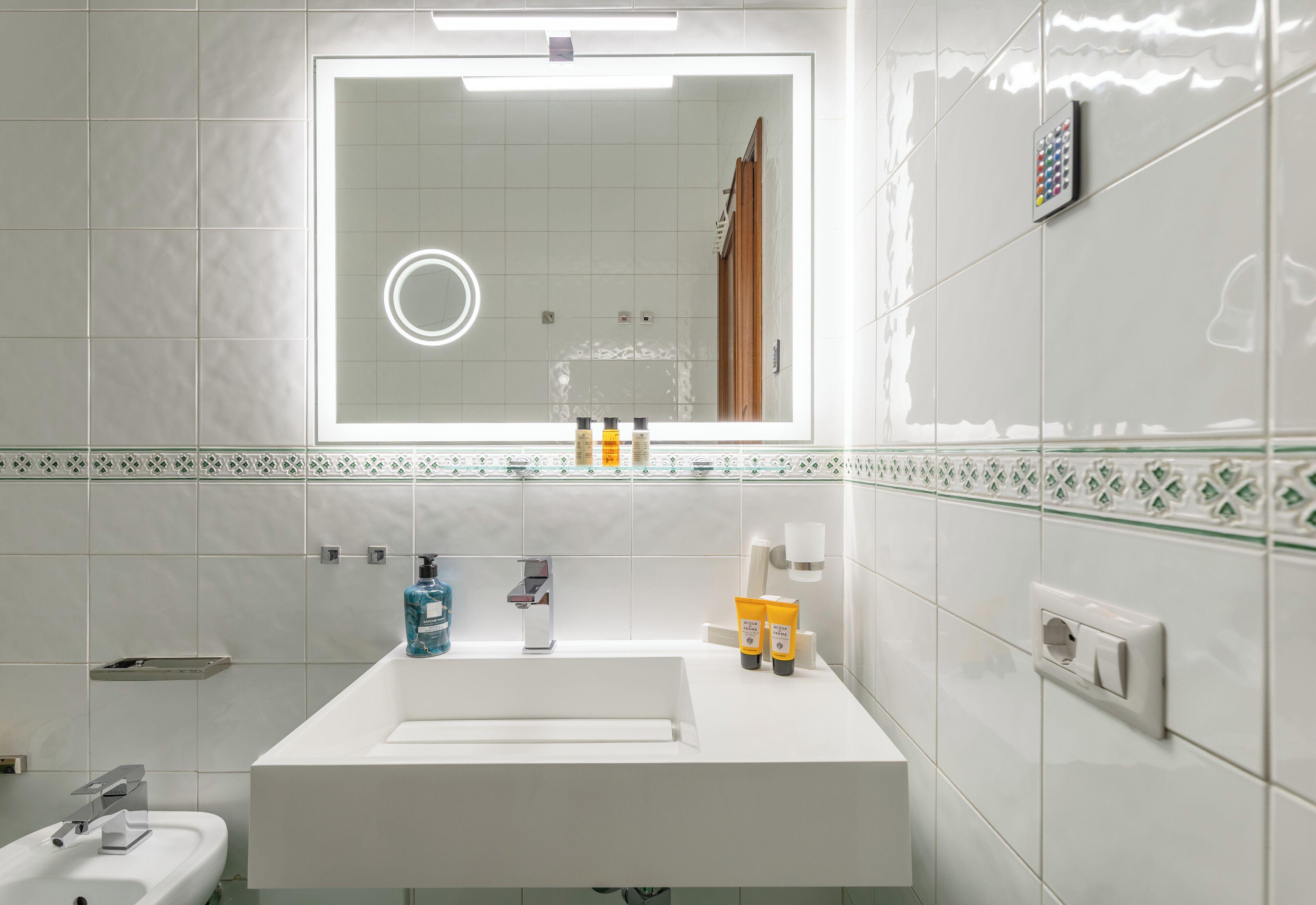 A modern bathroom with a large mirror, white sink, and toiletries.