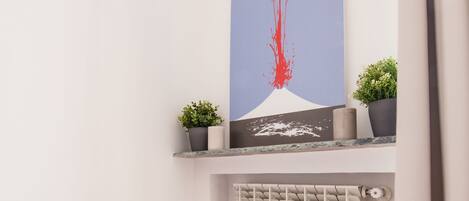 Un coin de pièce avec un radiateur blanc, un plancher en bois et une étagère sur laquelle sont posées deux plantes en pot et un tableau encadré.