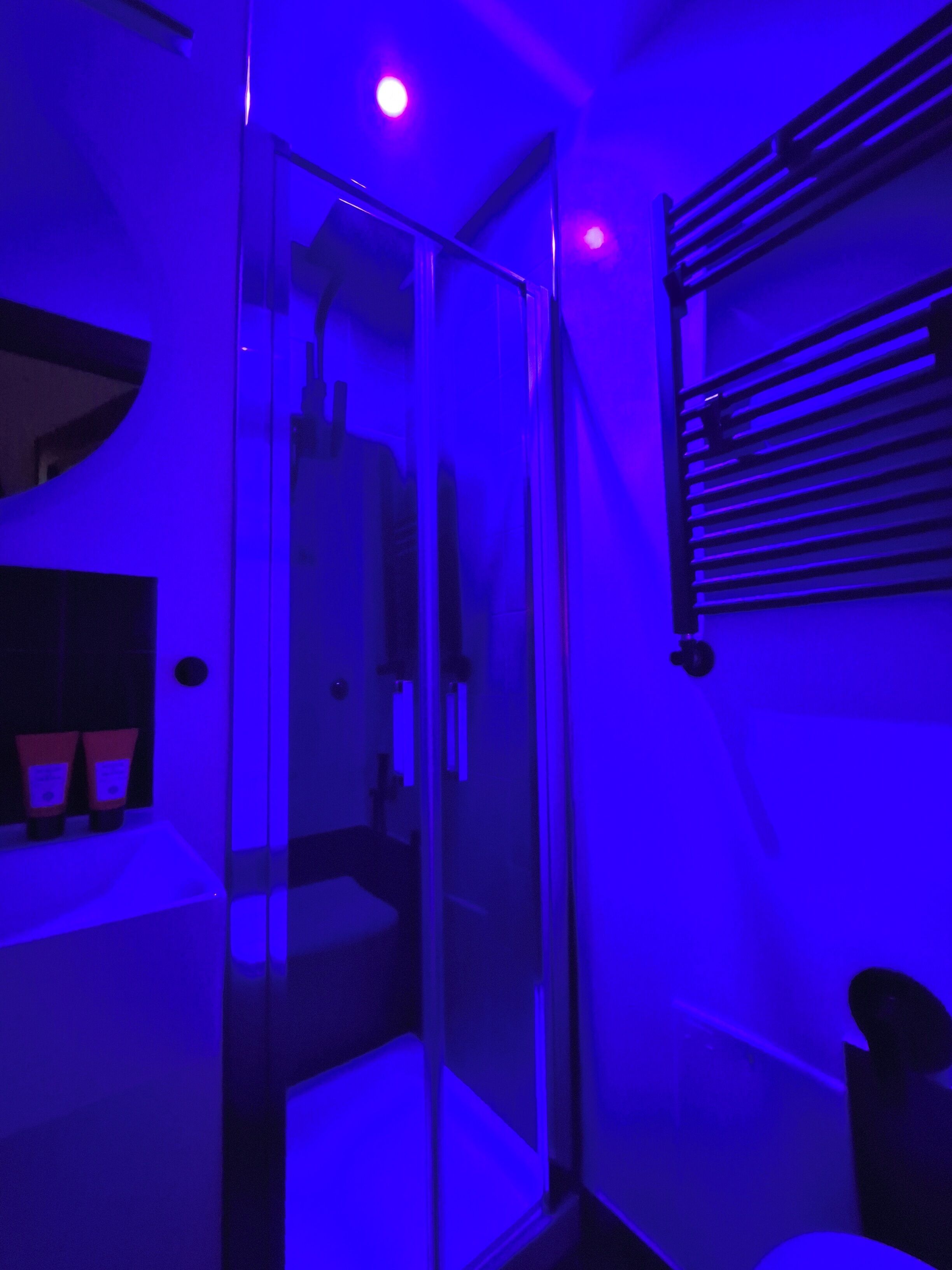Um quarto com divisória de vidro, uma cadeira preta e uma estante de metal na parede.