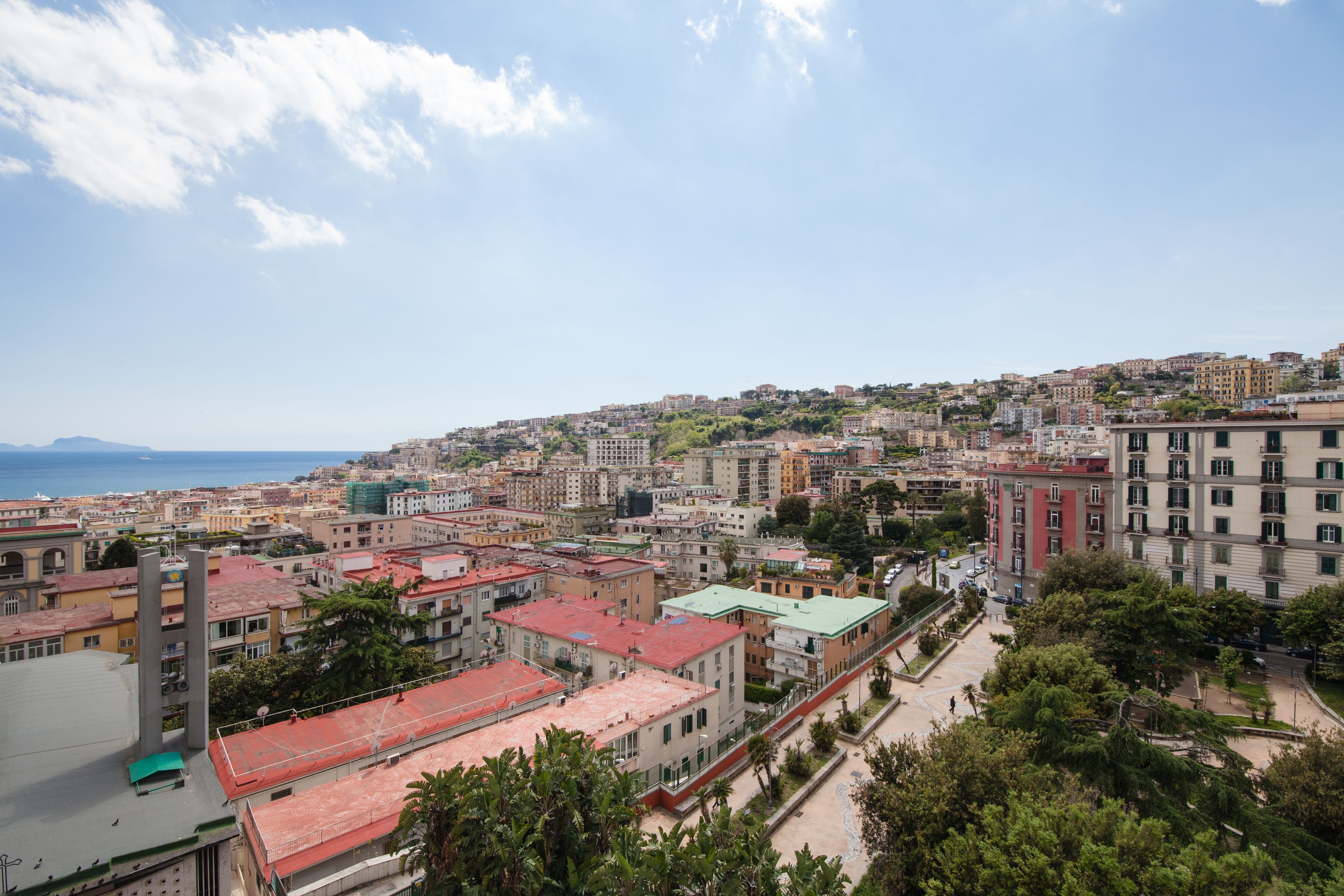 A cityscape with a mix of residential and commercial buildings, a prominent tower, and a view of the sea.