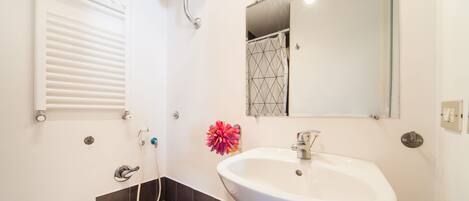 A bathroom with a white sink, a mirror, a shower, and a toilet.