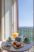 Een balkon met een ontbijtje, inclusief gebak, een kan sinaasappelsap en een groene theepot.