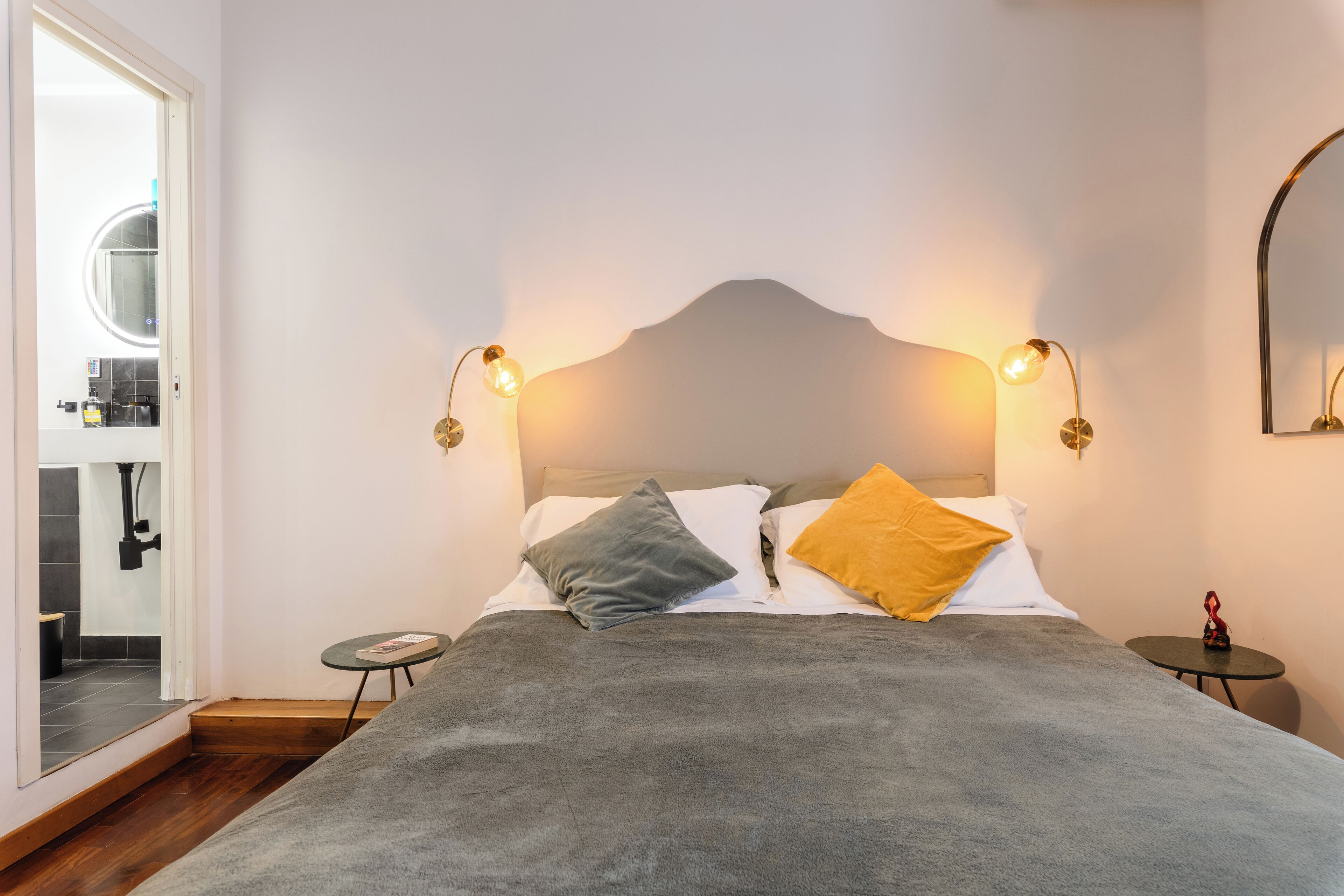 Ein Schlafzimmer mit einem großen Bett, zwei Nachttischen, einem Spiegel und einer Tür zu einem Badezimmer.