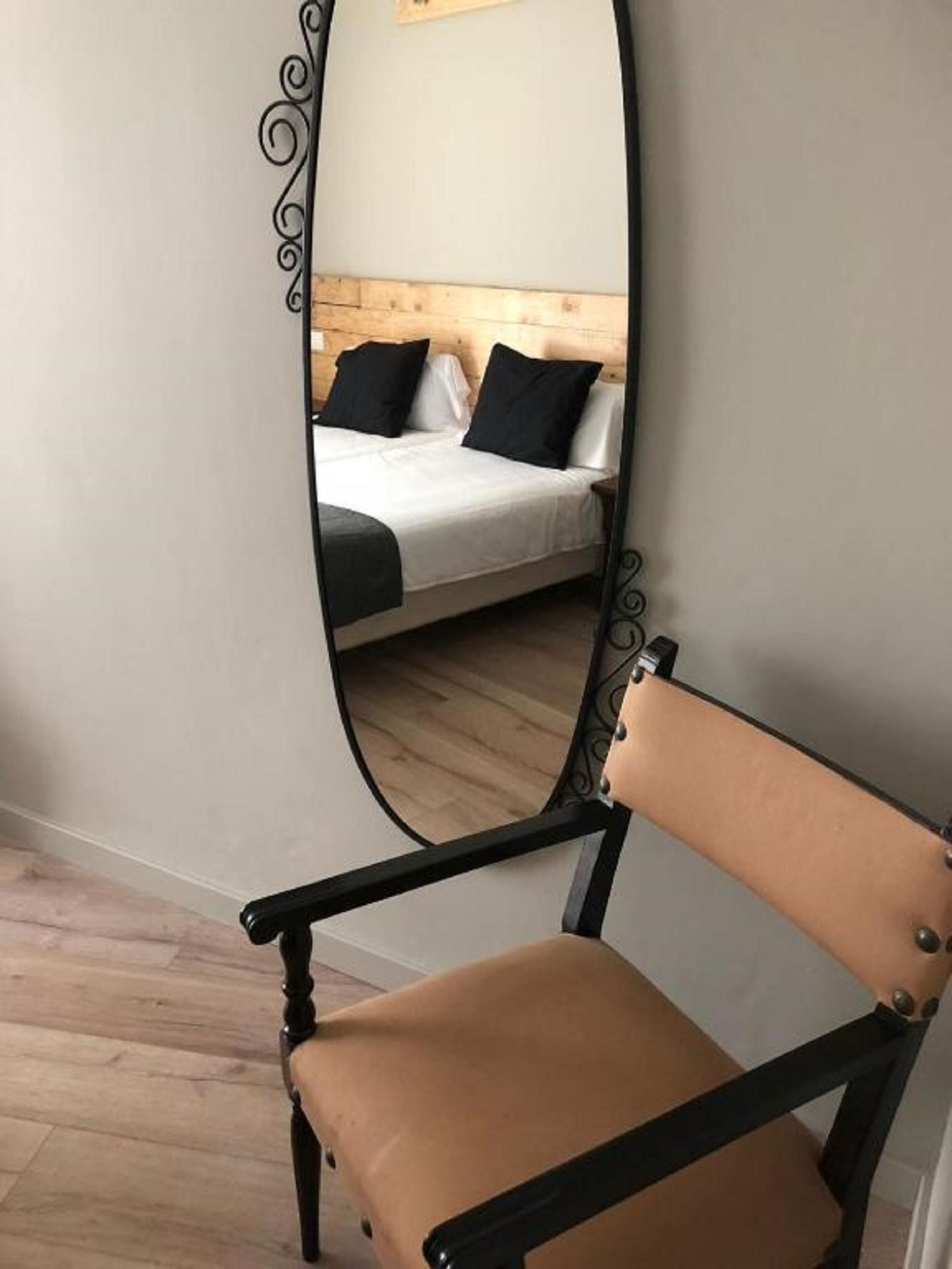 Een kamer met een bed, een stoel en een spiegel die het bed weerspiegelt.