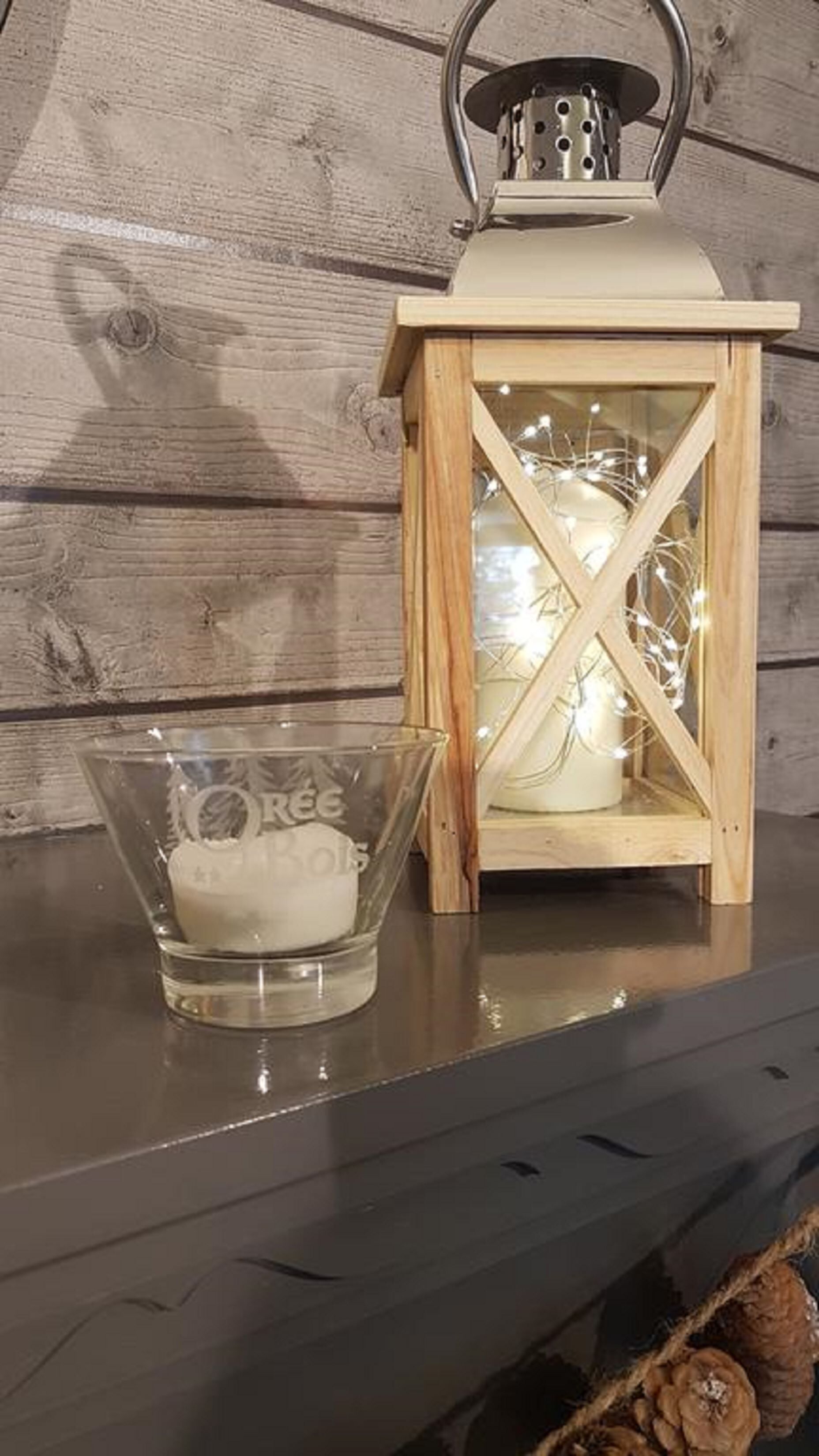 A wooden lantern with a glass enclosure and a candle inside, placed on a dark surface against a wooden background.