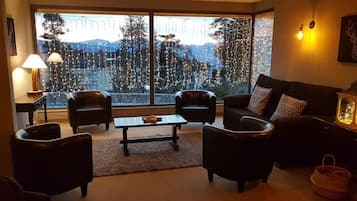 A cozy living room with a large window, two leather armchairs, a coffee table, and a sofa with patterned cushions.