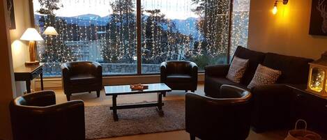 Ein gemütliches Wohnzimmer mit großem Fenster, zwei Ledersessel, einem Couchtisch und einer Couch mit gemusterten Kissen.