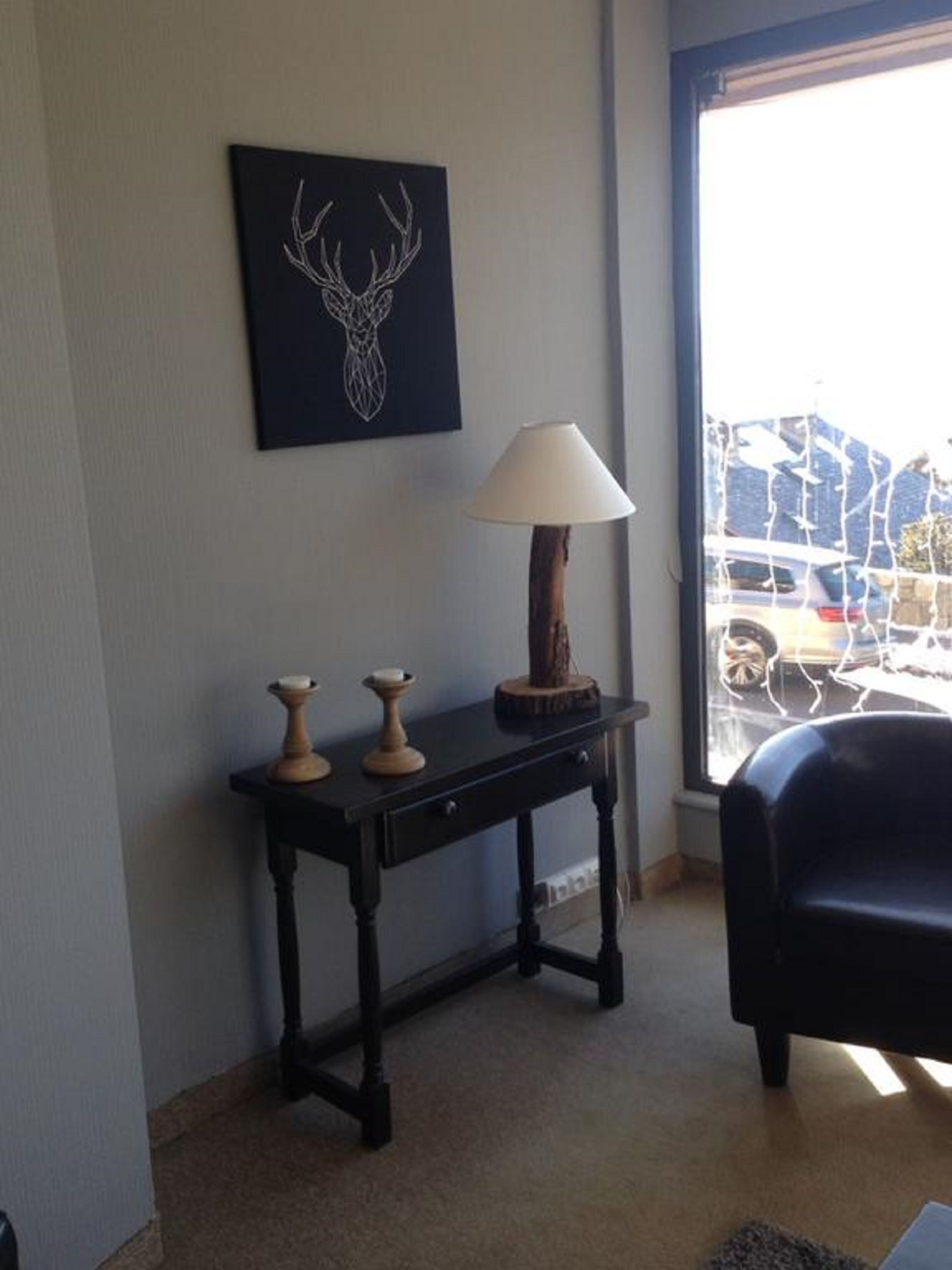 A room with a dark wooden table, a lamp, and a wall-mounted deer head artwork.