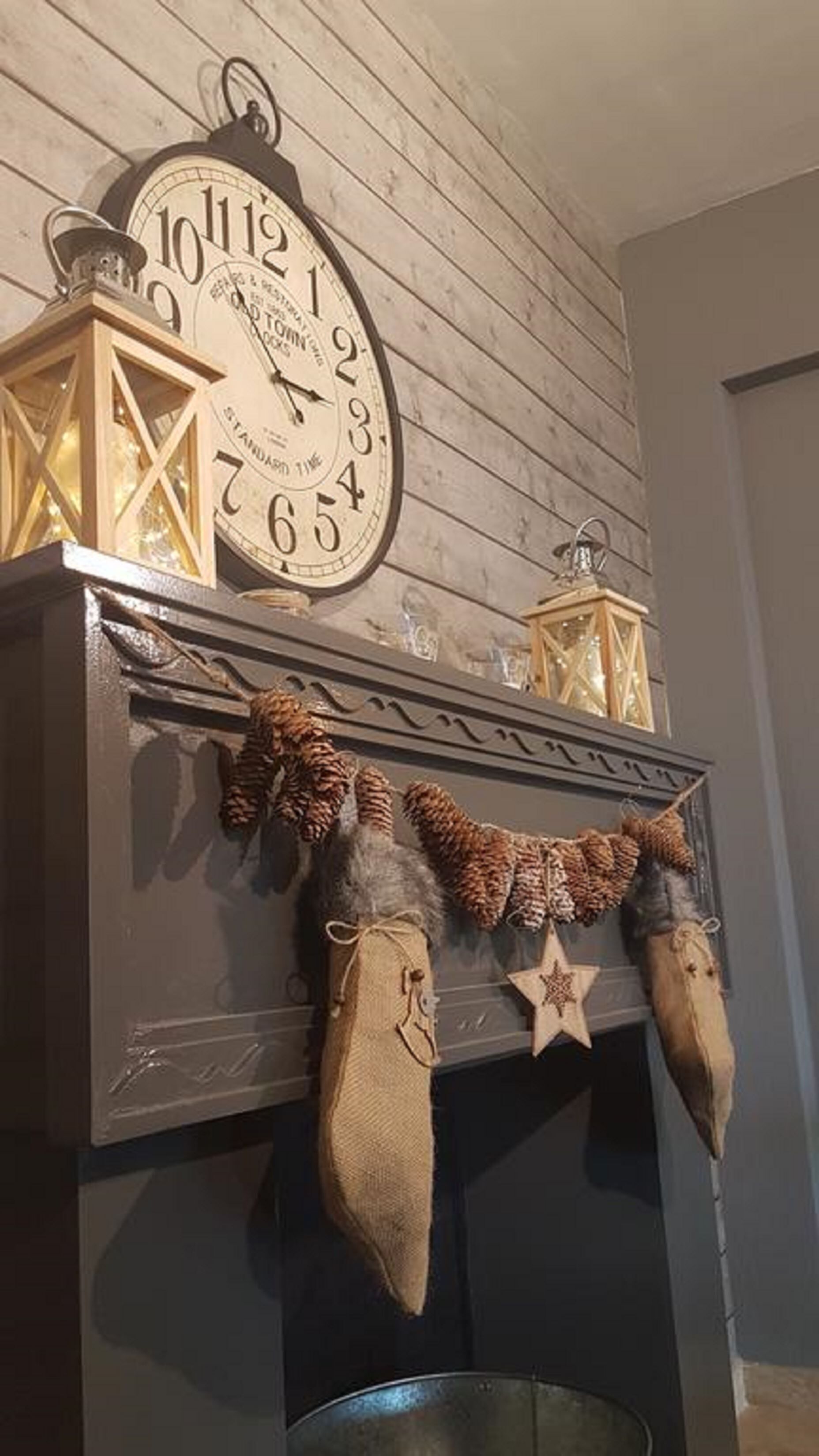 A fireplace with a clock above it, pine cones, and star-shaped decorations.