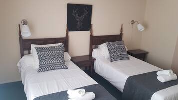 Een hotelkamer met twee bedden, elk voorzien van witte beddengoed en gestreepte kussens. Daarboven hangt een kunstwerk van een hertenhoofd aan de muur.