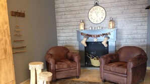 Een gezellige kamer met twee leren fauteuils, een houten buffetkast, een rustieke open haard en een wandklok.