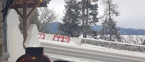 A wooden table with a vase and a chair, a stone wall, and a view of a snowy landscape with trees and a road.