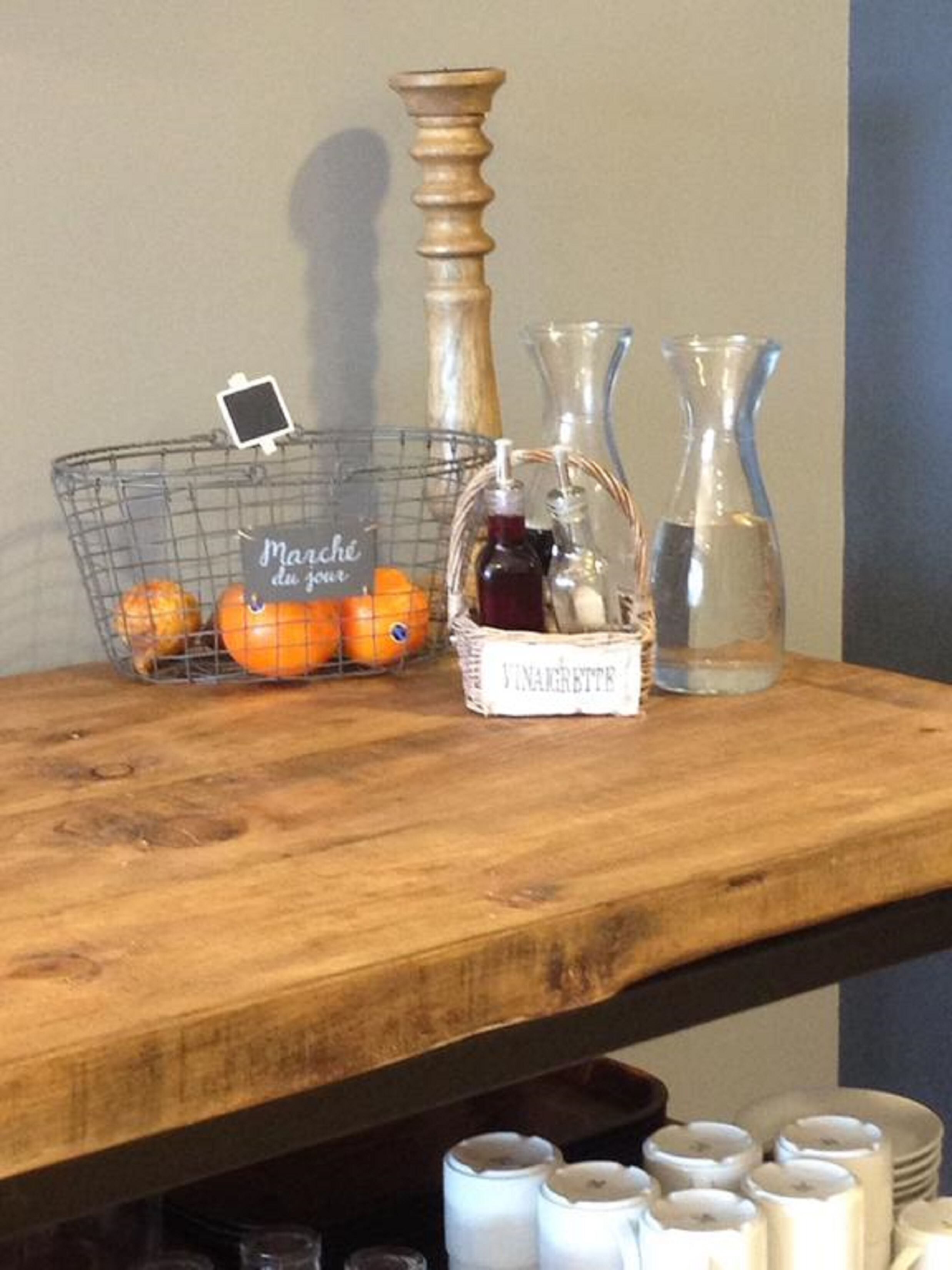 A wooden shelf with a wire basket labeled "Marché du Jour," containing oranges and a small photo frame. There are two glass vases and a white container with "Vin Maréchal" written on it.