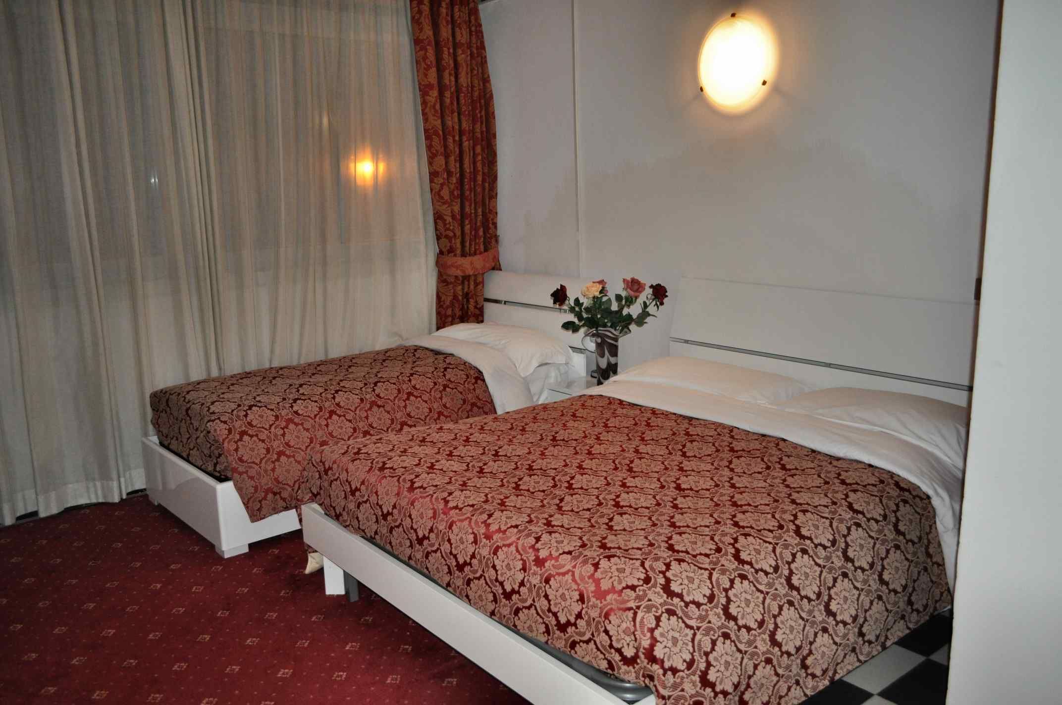 Ein Hotelzimmer mit zwei Betten, einer Blumenvase und einer Wandleuchte.