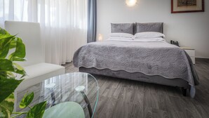 Una habitación de hotel moderna con cama, mesita de noche, sillón y mesa de vidrio.