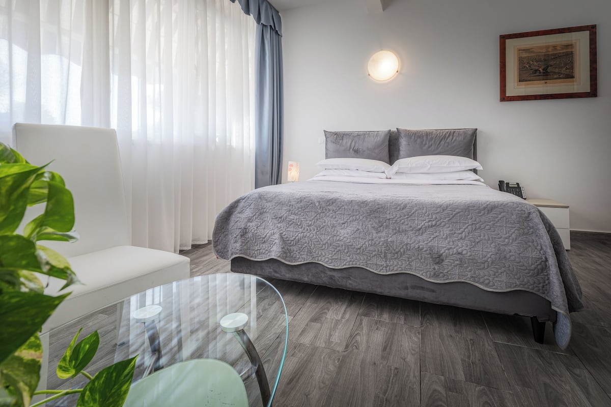 Una habitación de hotel moderna con cama, mesita de noche, sillón y mesa de vidrio.