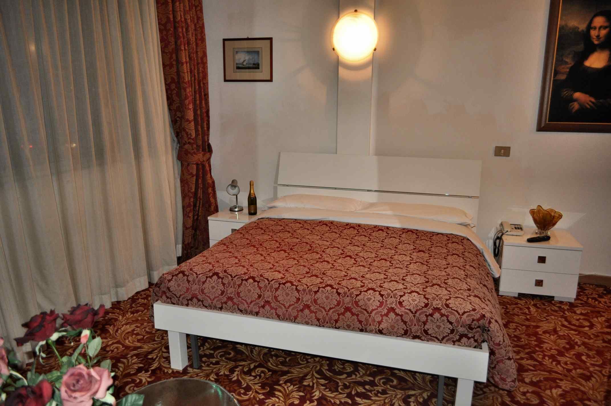 Une chambre à coucher bien rangée, avec un lit, des tables de chevet, une petite table et une lampe fixée au mur.