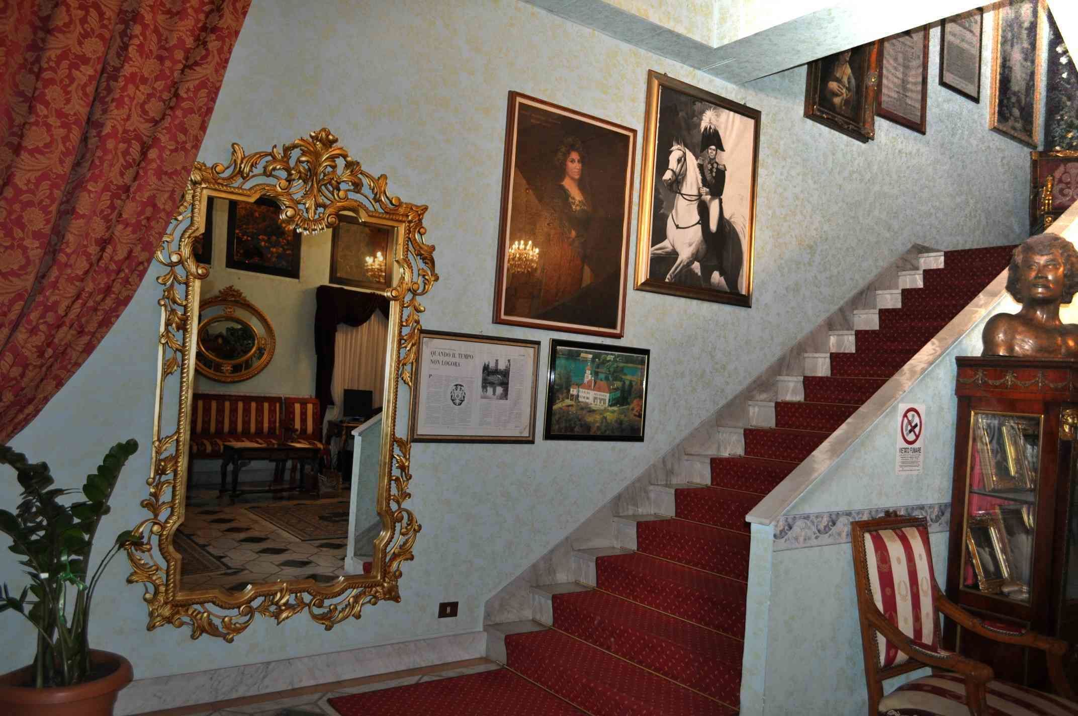 A staircase with red carpeted steps, a large ornate mirror, and framed pictures on the walls.
