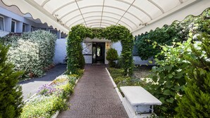 Un sendero cubierto que lleva a la entrada de un edificio, rodeado de vegetación exuberante y plantas con flores.