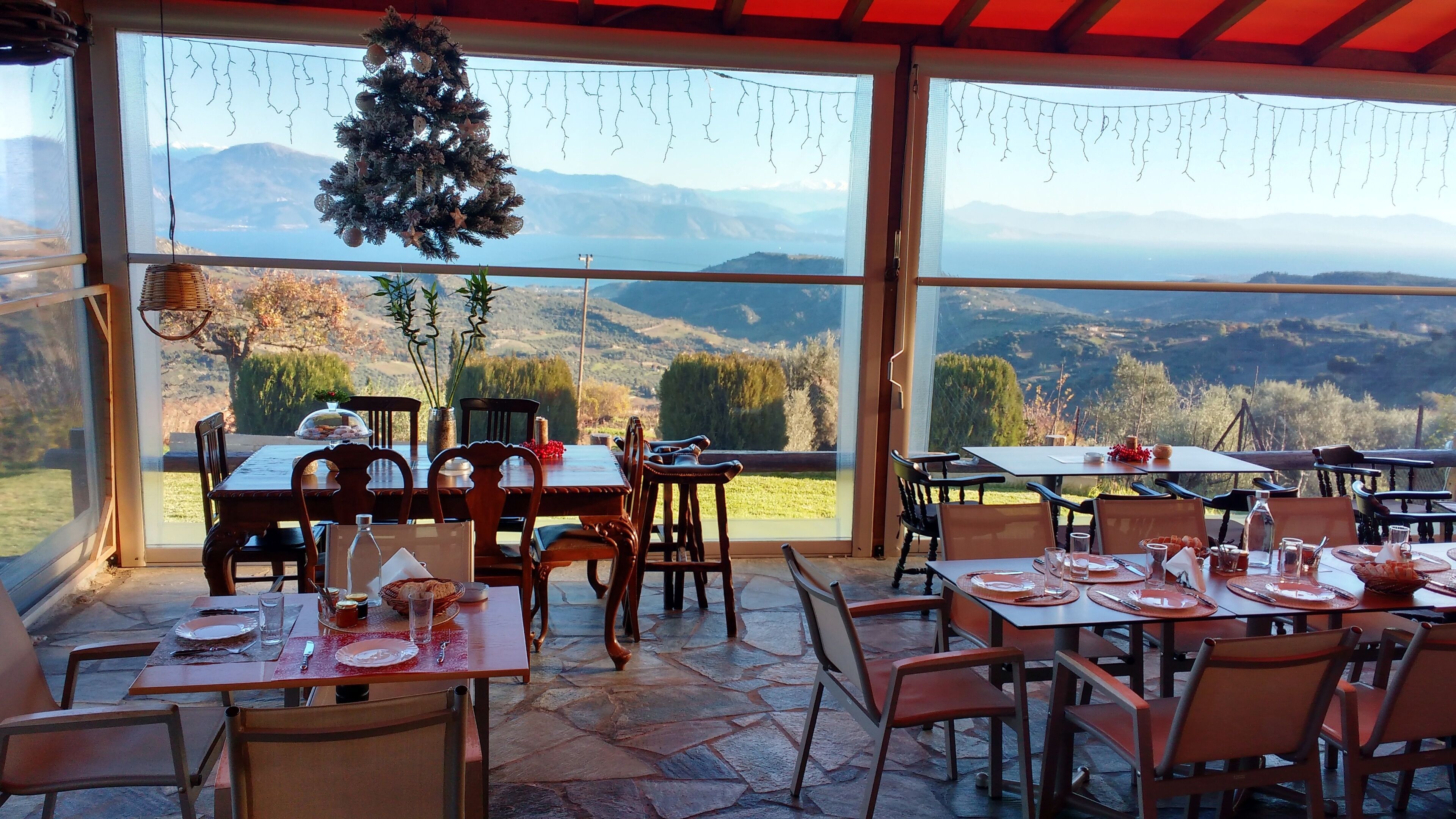An outdoor dining area with tables and chairs, a Christmas tree, and a view of mountains and a lake.