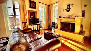Una sala de estar con sofá de cuero, televisión, chimenea y ventanas amplias.