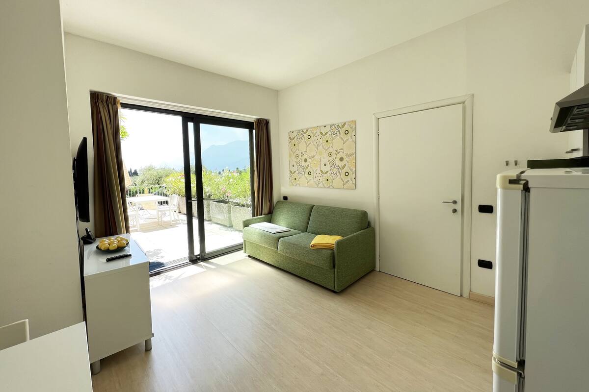 Una sala de estar moderna y minimalista con un sofá verde, un televisor de pantalla plana y un comedor con una mesa y sillas.
