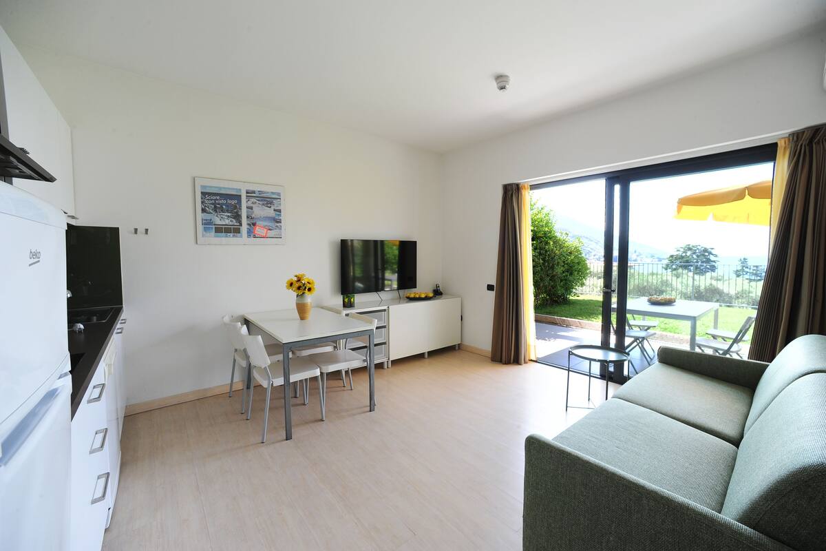 Una sala de estar moderna con un sofá, una mesa de comedor con sillas, un televisor y una zona de cocina con un refrigerador.