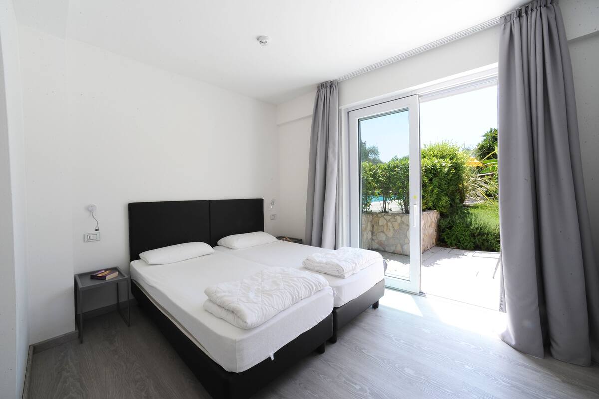 Un dormitorio moderno con una cama grande, una mesita de noche y un ventanal corredero que da a un balcón.