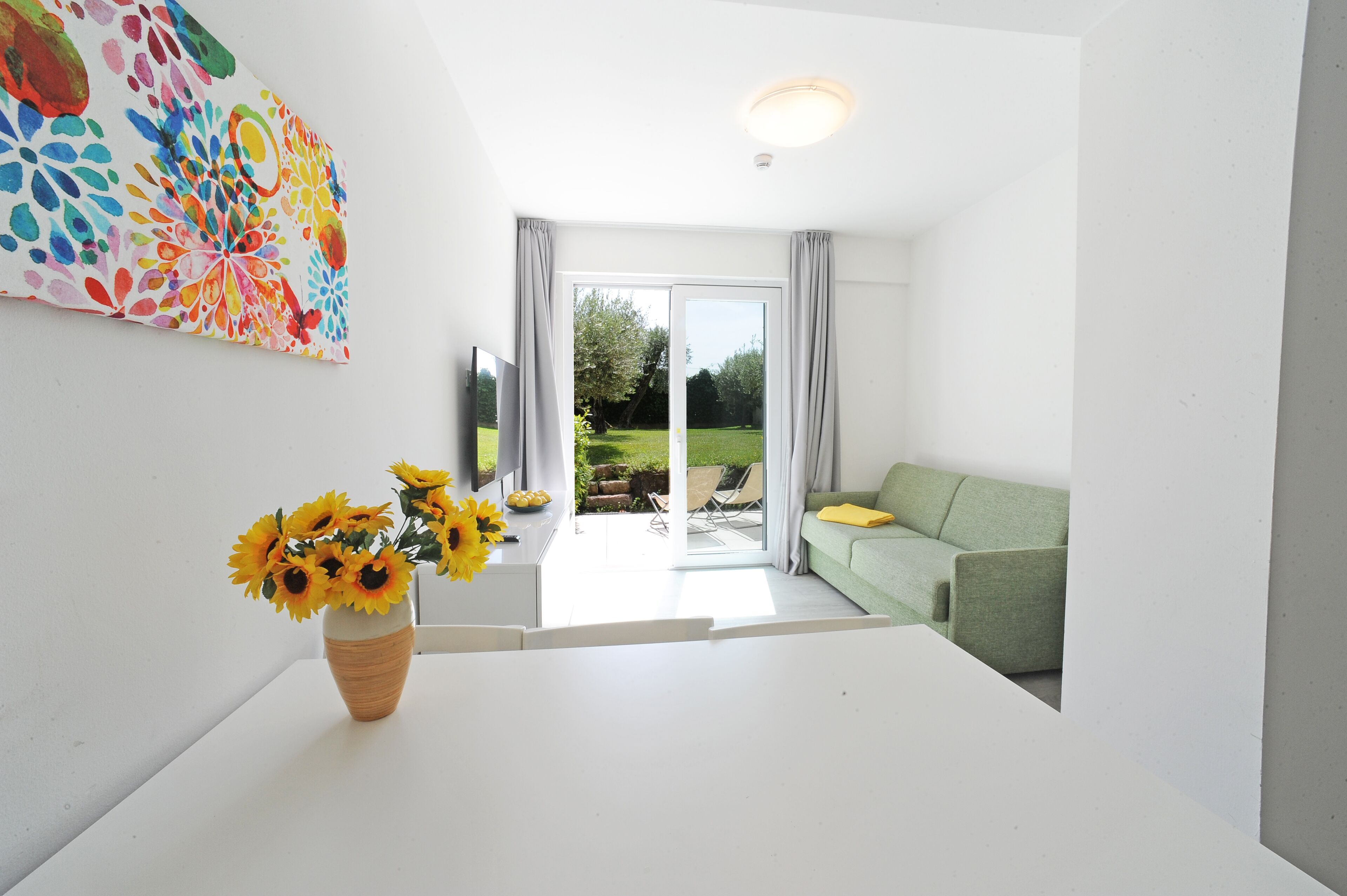 A modern living room with a white table, a green sofa, and a large window with curtains.