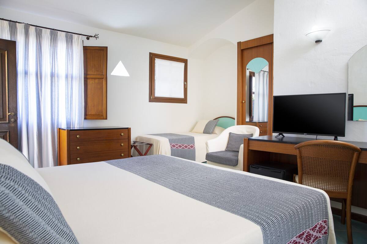 A hotel room with a bed, a desk, a television, a chair, and a wardrobe.