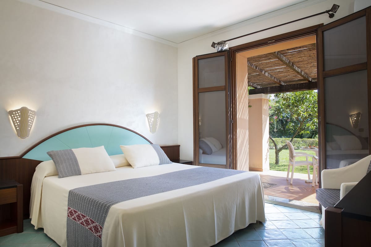 A bedroom with a bed, a nightstand, a chair, and a view of the outside.