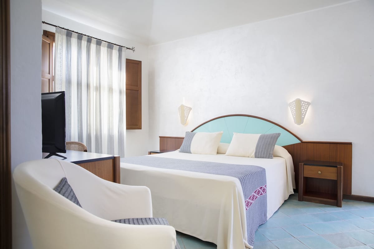 A hotel room with a bed, two bedside tables, a chair, a TV, and curtains.