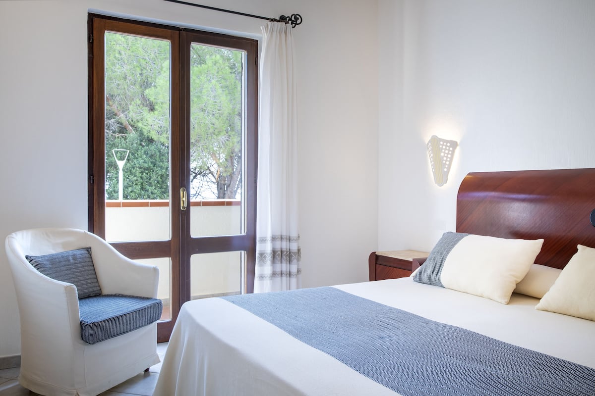 A bedroom with a bed, a chair, a nightstand, and a window with curtains.