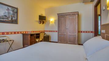 A hotel room with a bed, desk, chair, wardrobe, and a painting on the wall.