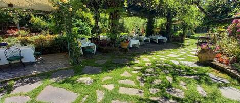 An outdoor garden with stone pathways, tables, and chairs arranged for dining.