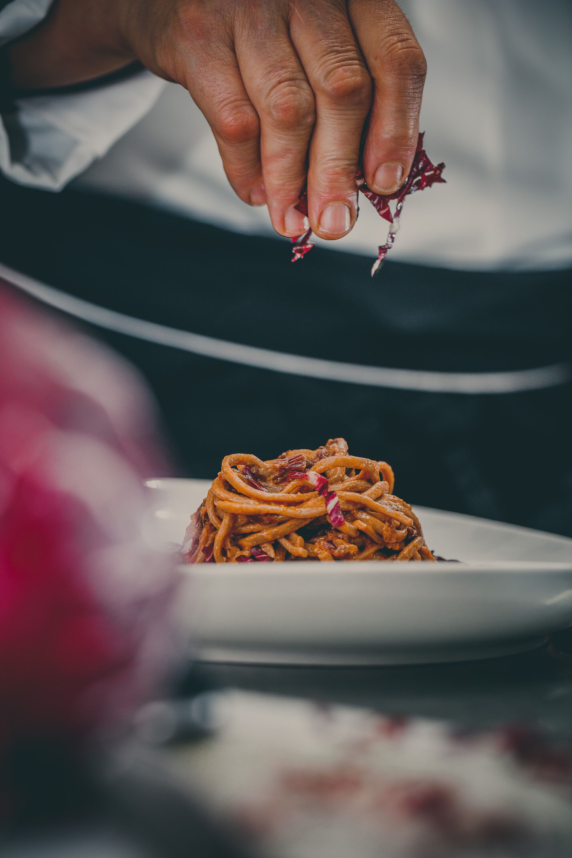 A hand sprinkling a garnish over a plate of spaghetti.