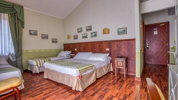 A hotel room with two beds, wooden flooring, a wooden headboard, a nightstand, and a door with a sign.