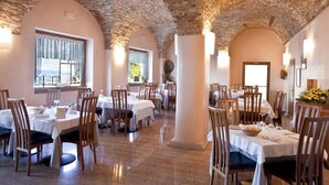 A restaurant with stone arches, white tables, and wooden chairs. - Hotel Pai (Torri del Benaco)